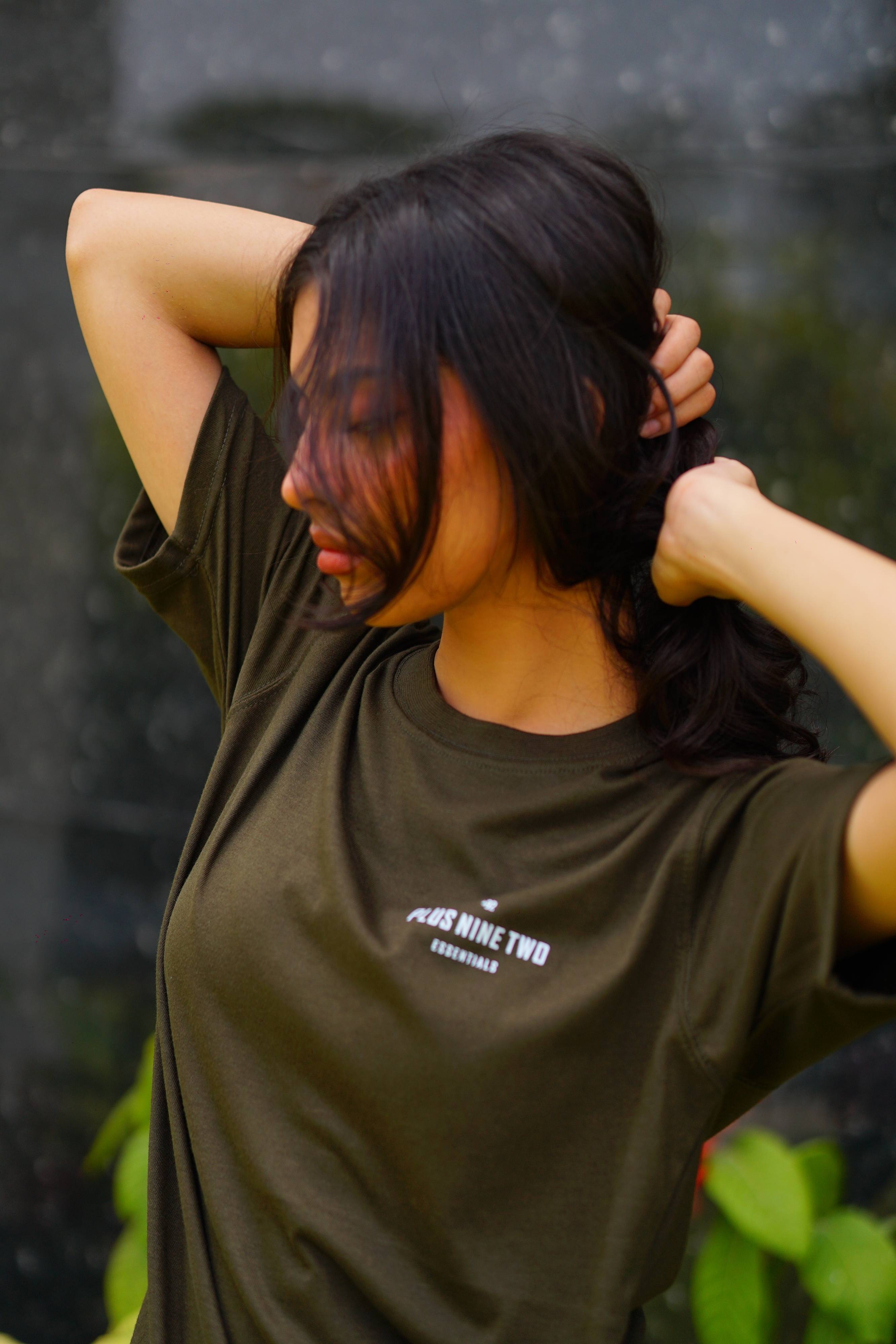 Girl wearing essentials blend army green t-shirt holding her hair with the pocket design visible.