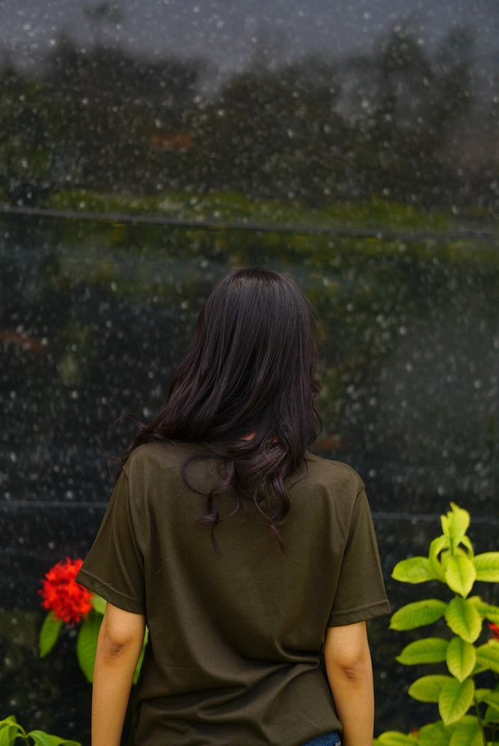 Girl wearing essentials blend army green t-shirt facing against the camera to show the fit from the back.