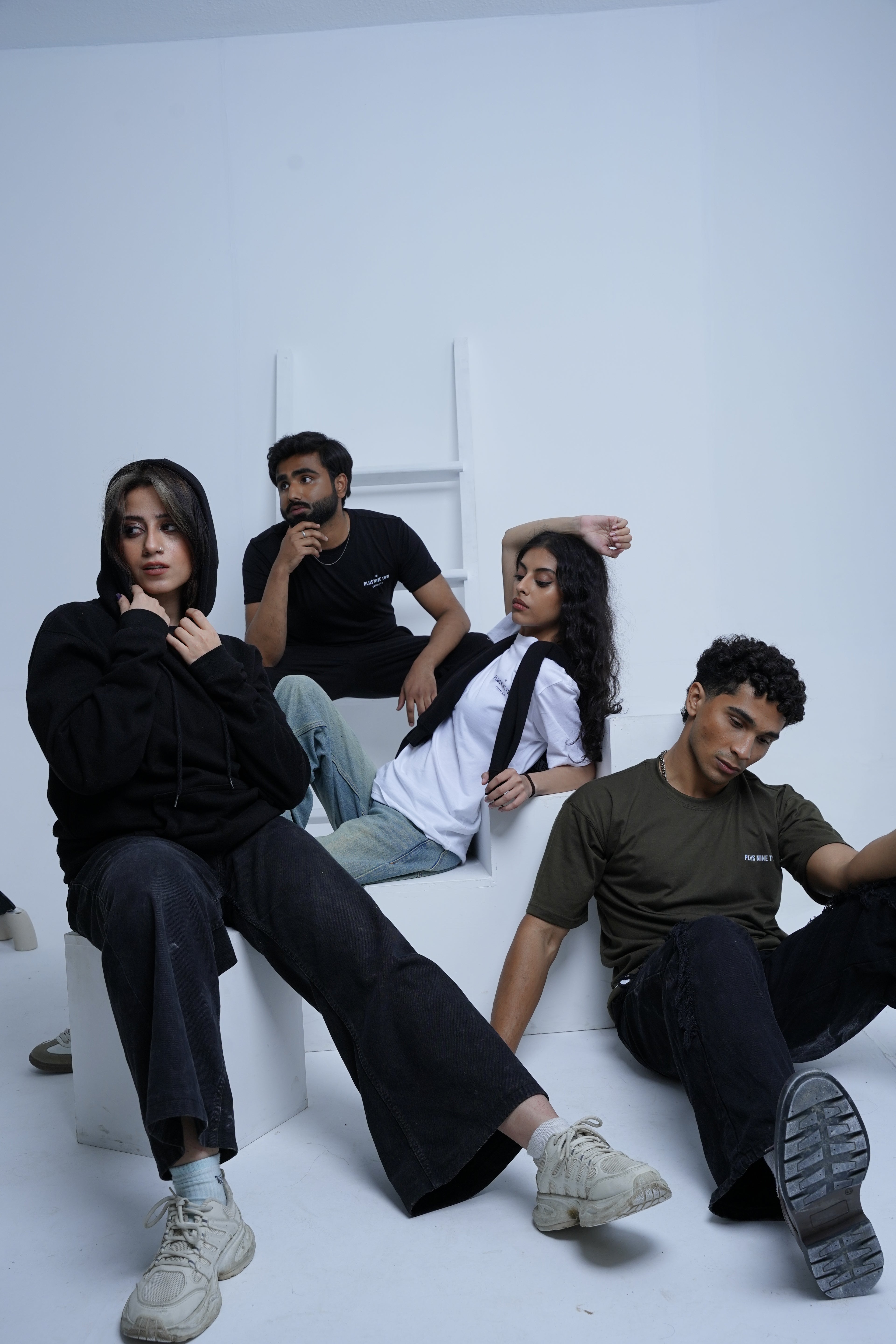Four people arranged in a circle on a white floor with a white wall background wearing plus92 clothing