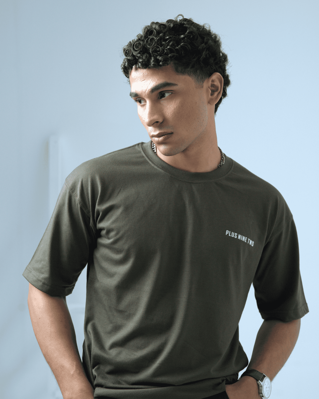 Man wearing an army green oversized t-shirt with the logo 'PLUS NINE TWO' on a light background