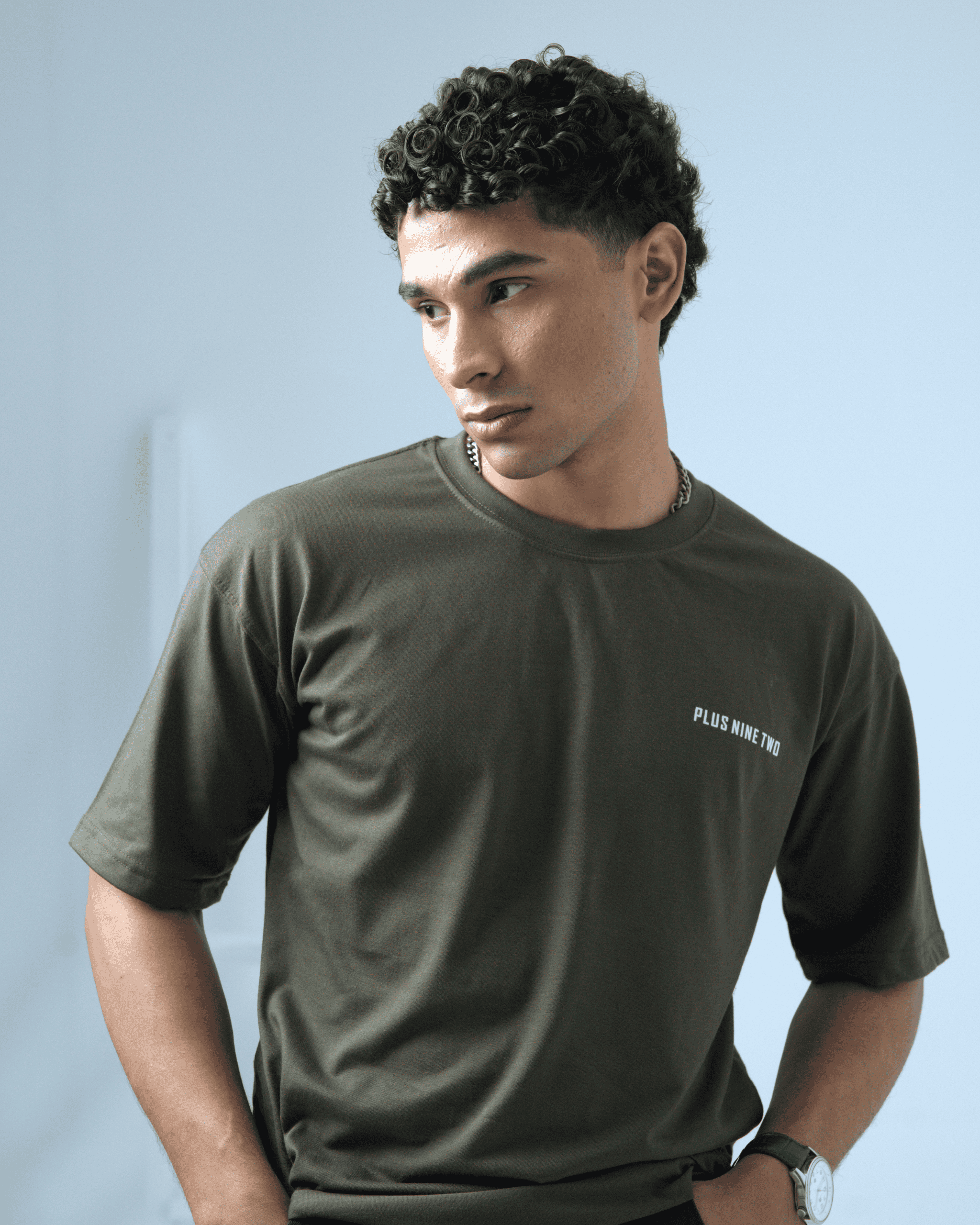 Man wearing an army green oversized t-shirt with the logo 'PLUS NINE TWO' on a light background