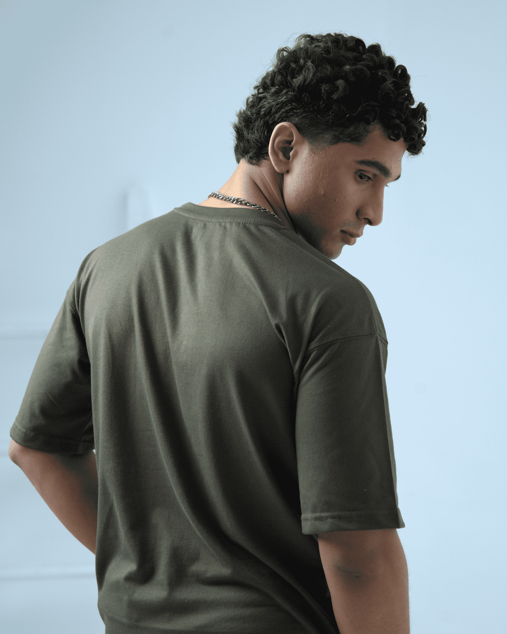 Man wearing an army green oversized t-shirt facing away from the camera against a light background
