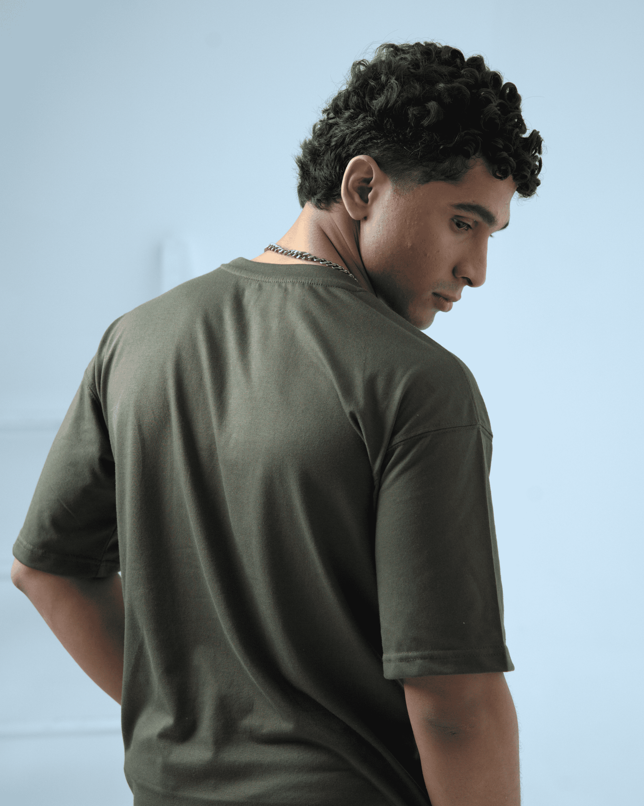 Man wearing an army green oversized t-shirt facing away from the camera against a light background