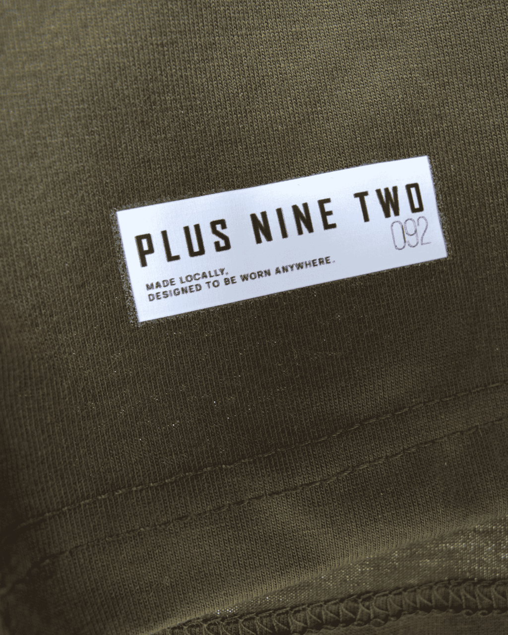 Label with 'PLUS NINE TWO' text on army green oversized t-shirt.