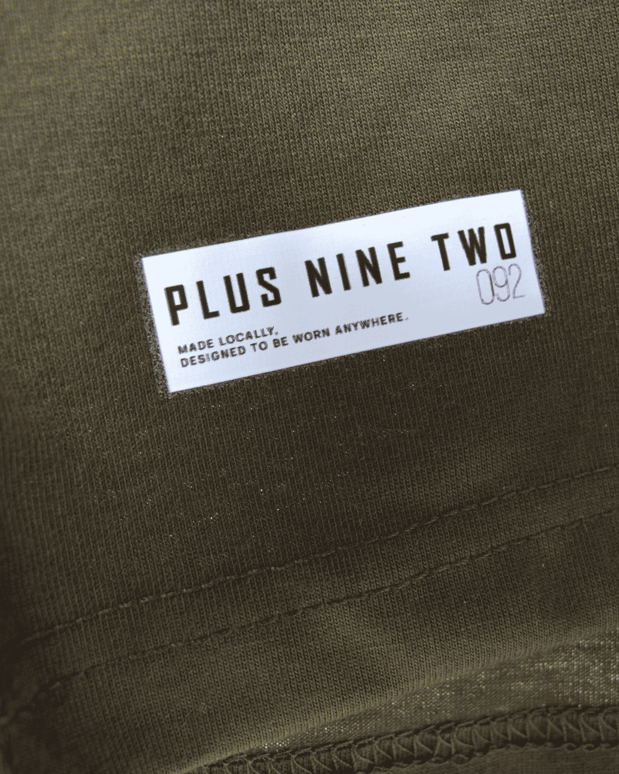 Label with 'PLUS NINE TWO' text on army green oversized t-shirt.