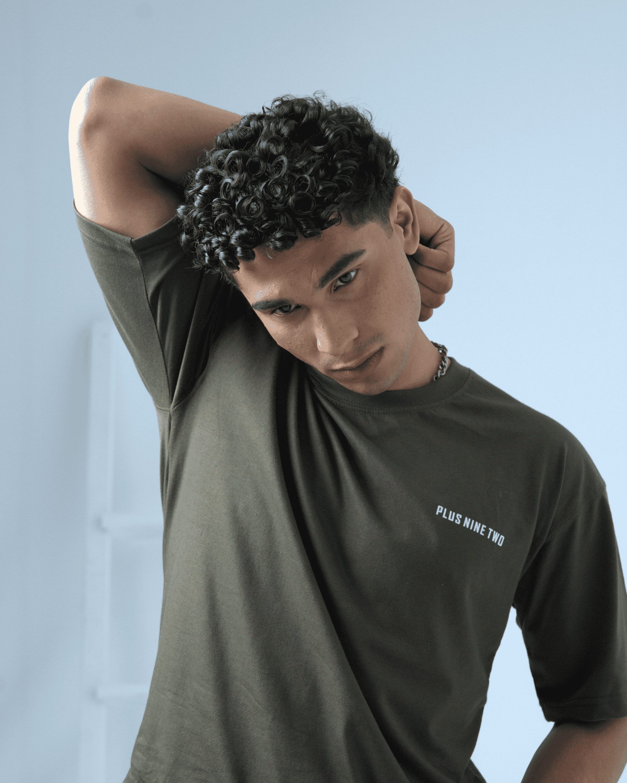 Man wearing an army green t-shirt with text 'PLUS NINE TWO' on a light background