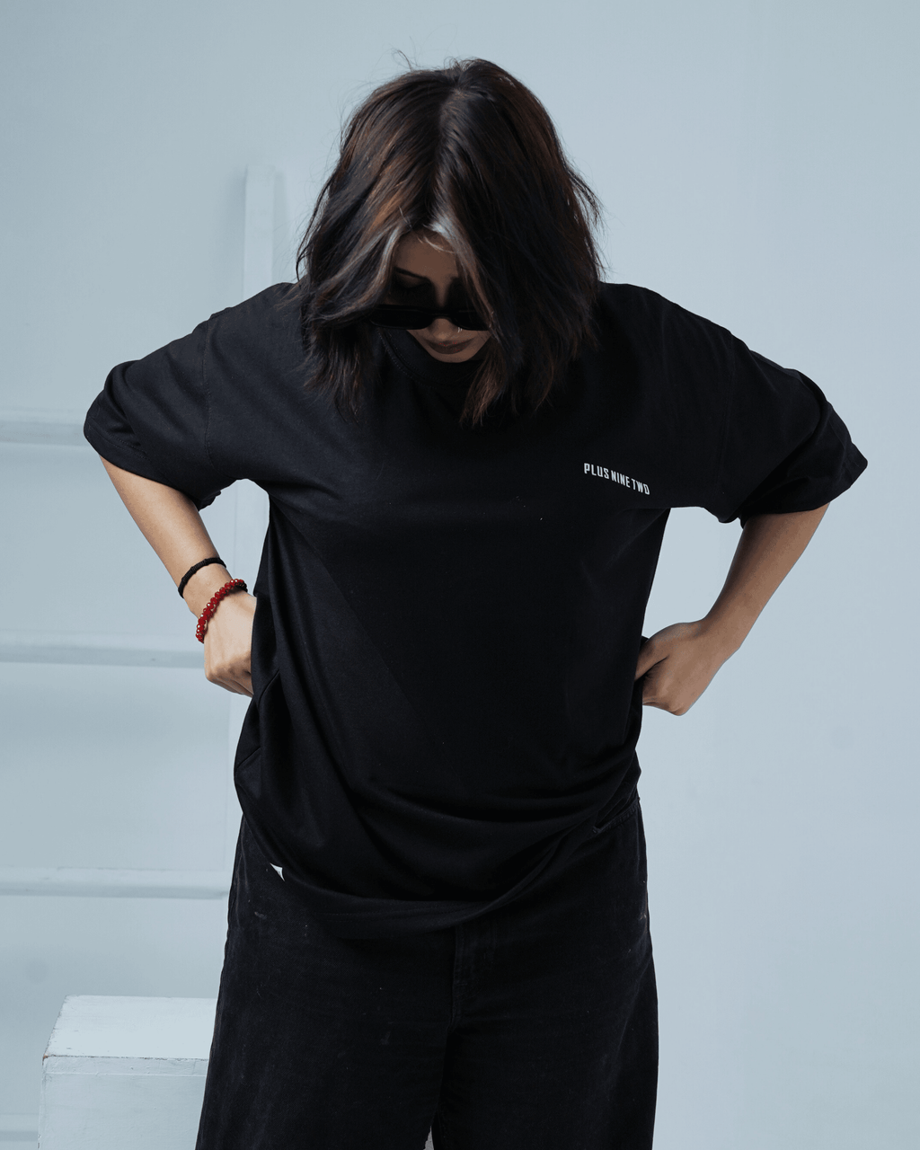 Woman wearing a black t-shirt with text 'PLUS NINE TWO' on a light background