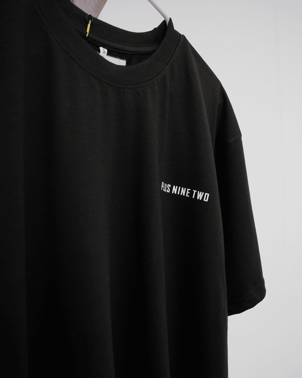 Black t-shirt with white text 'PLUS NINE TWO' on a hangar.