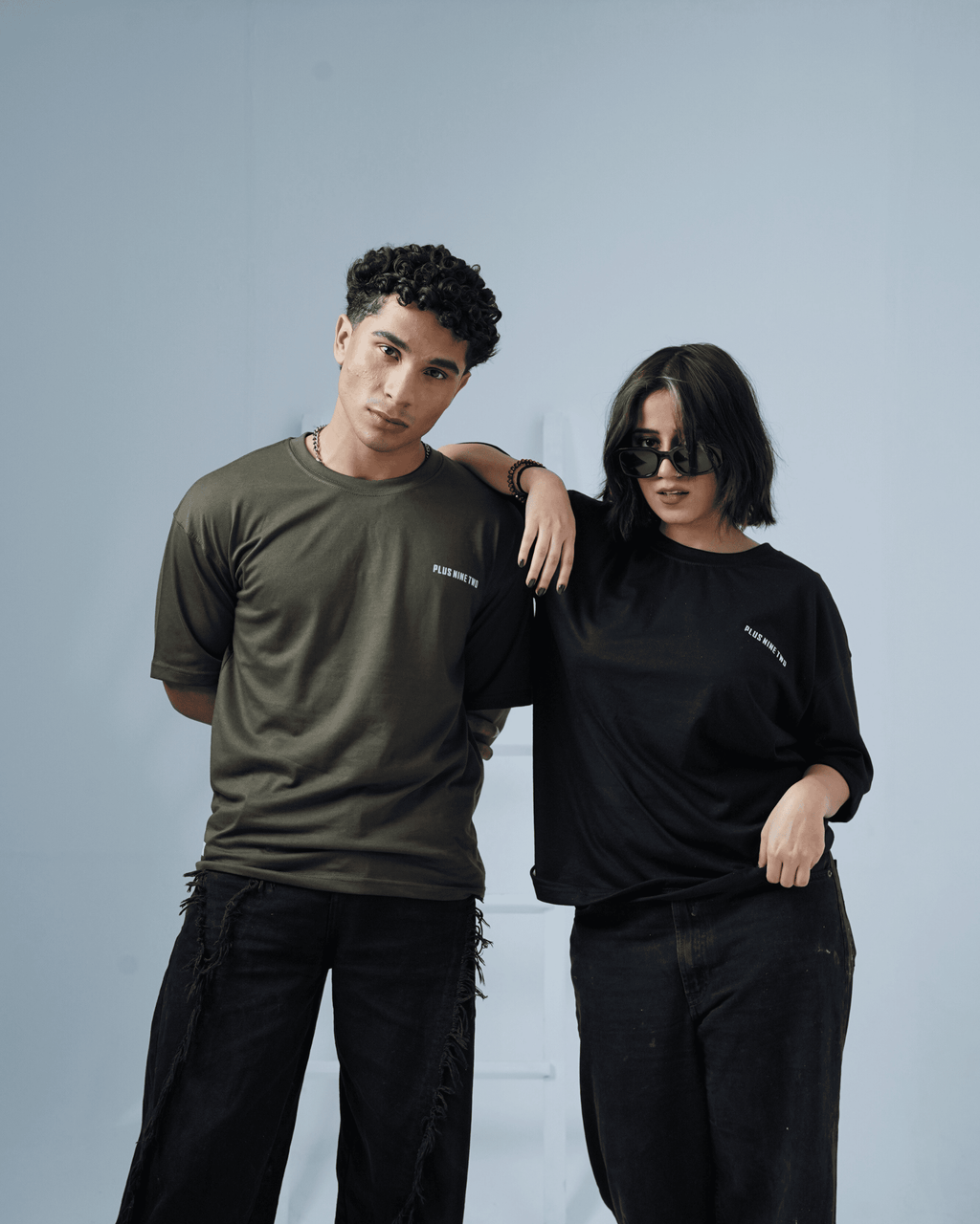 Two people a man and a woman wearing army green and black plus92clothing oversized t-shirts against a plain background