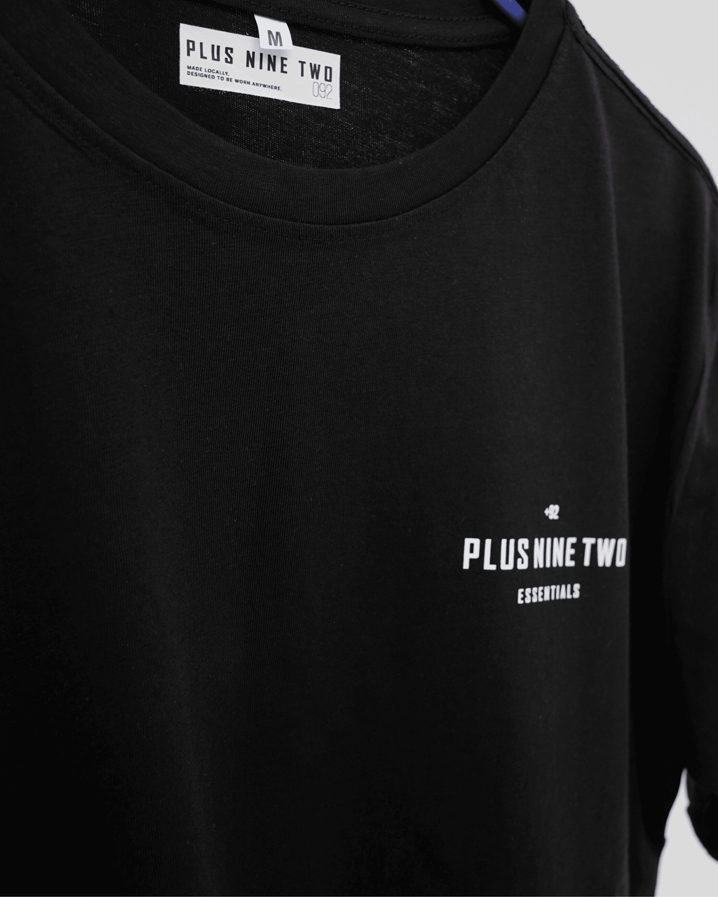 Black t-shirt with 'Plus Nine Two' logo on a gray background