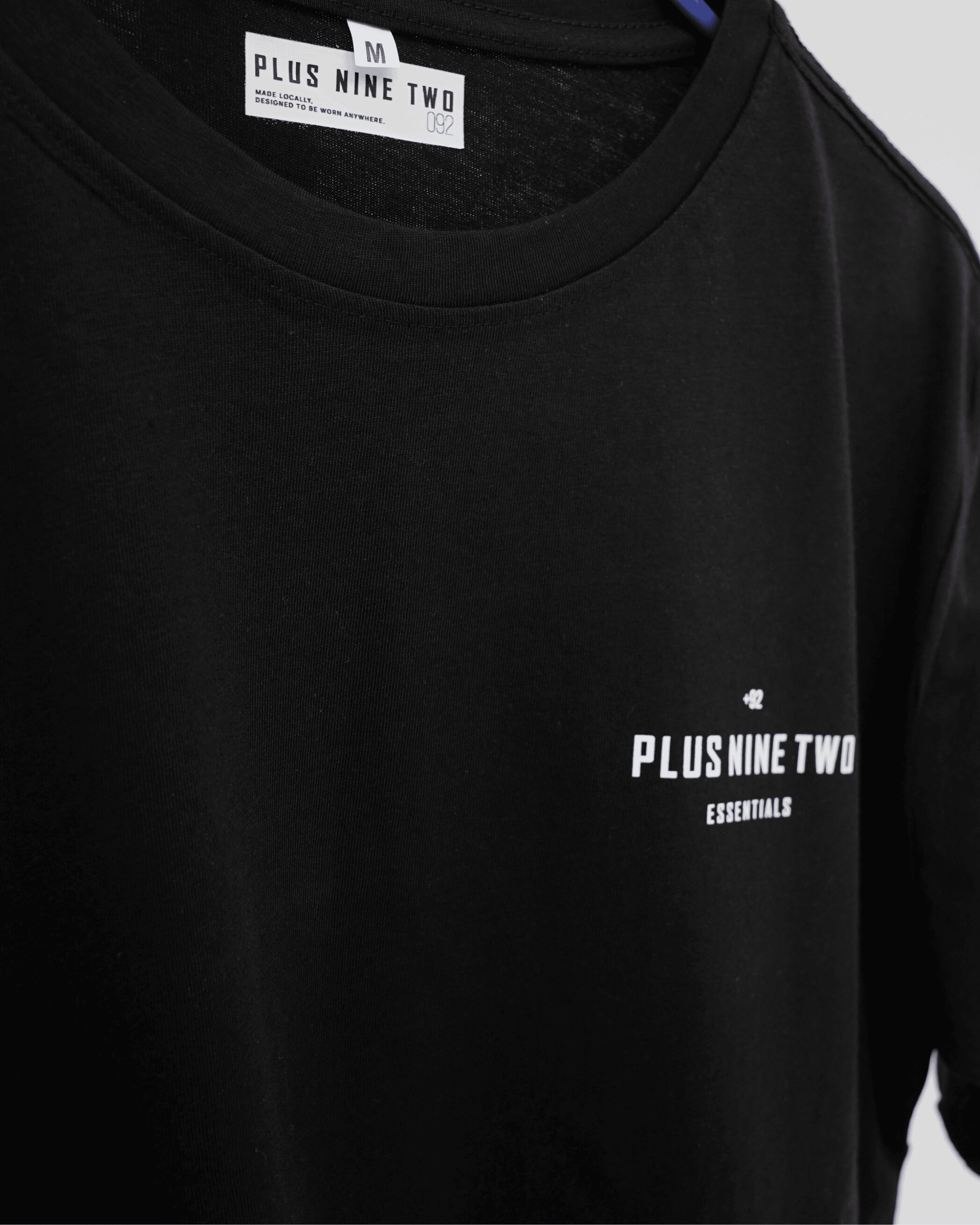 Black t-shirt with 'Plus Nine Two' logo on a gray background