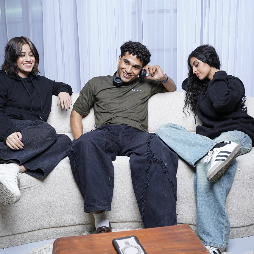 Three people sitting on a couch with a neutral background wearing plus92 clothing