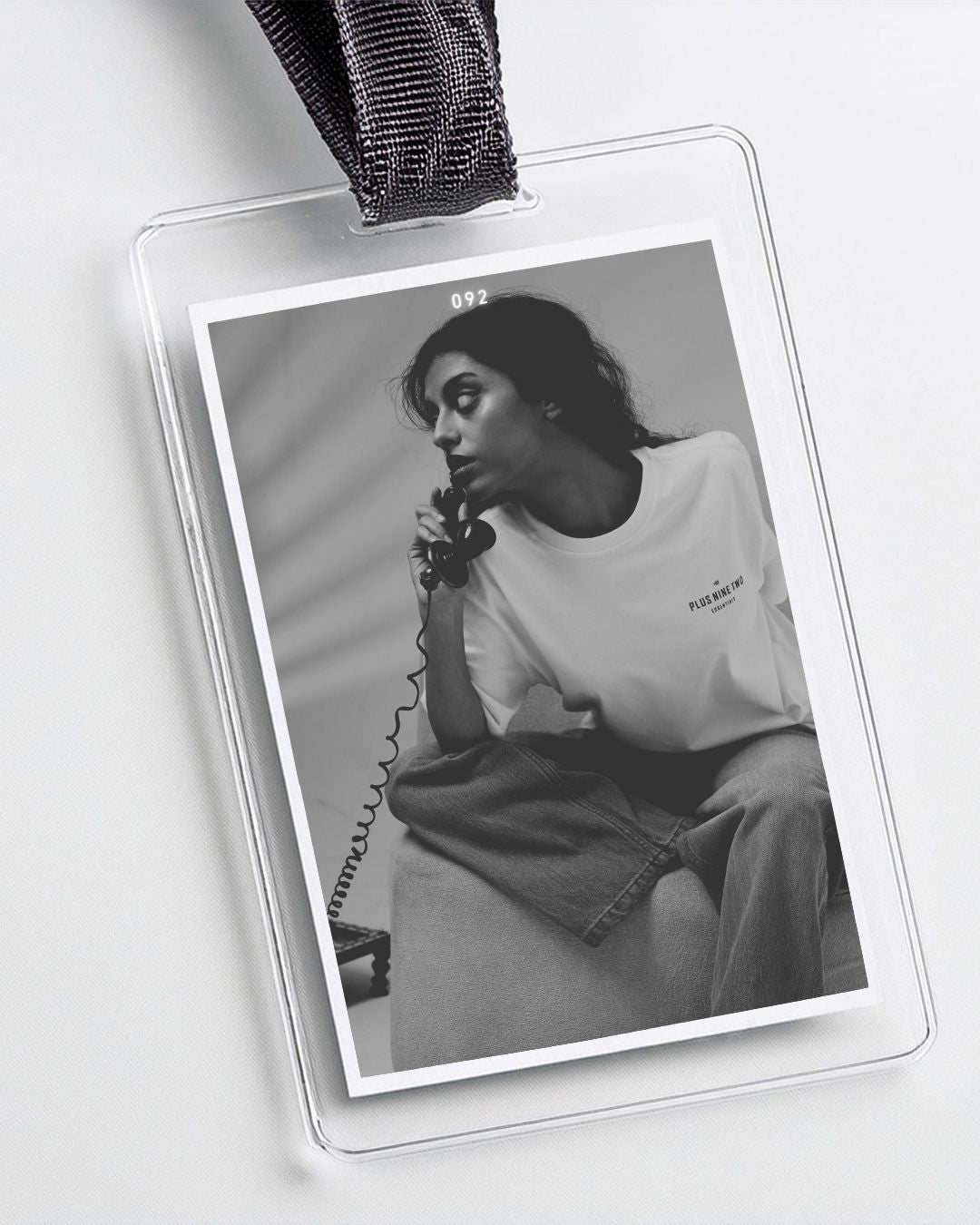 Black and white photo of a woman wearing the white essentials t-shirt with text 092 titled as the card number, held in a badge holder.