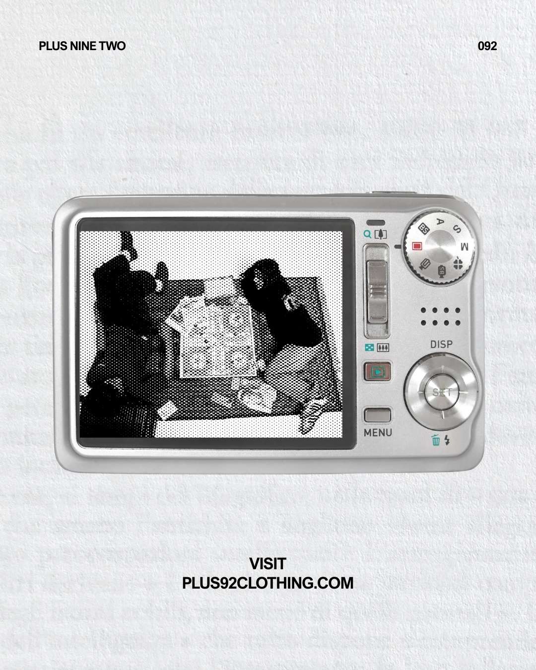 Digital camera with a screen displaying a black and white image of people playing cards, on a textured light gray background wearing plus92 clothing