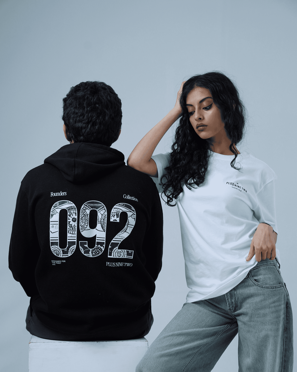Two people, man facing away wearing founders hoodie and a women wearing a white t-shirt with text on a gray background.