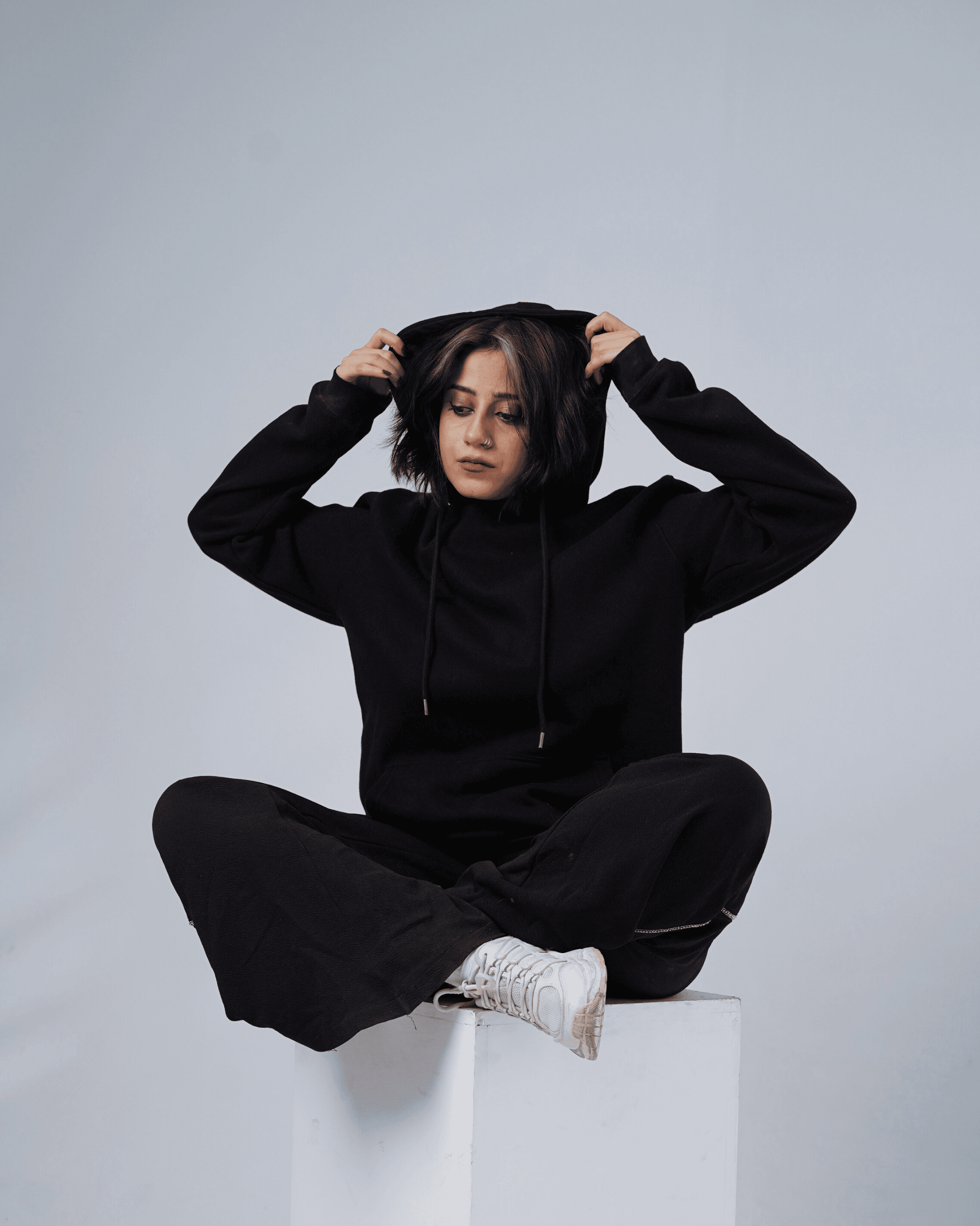 Person wearing a black founders hoodie and sitting on a white block against a light background
