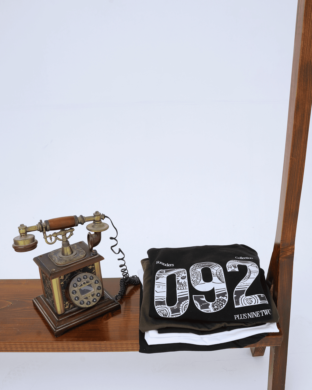 Vintage-style phone and black founders hoodie folded above other +92clothing products on a wooden surface.
