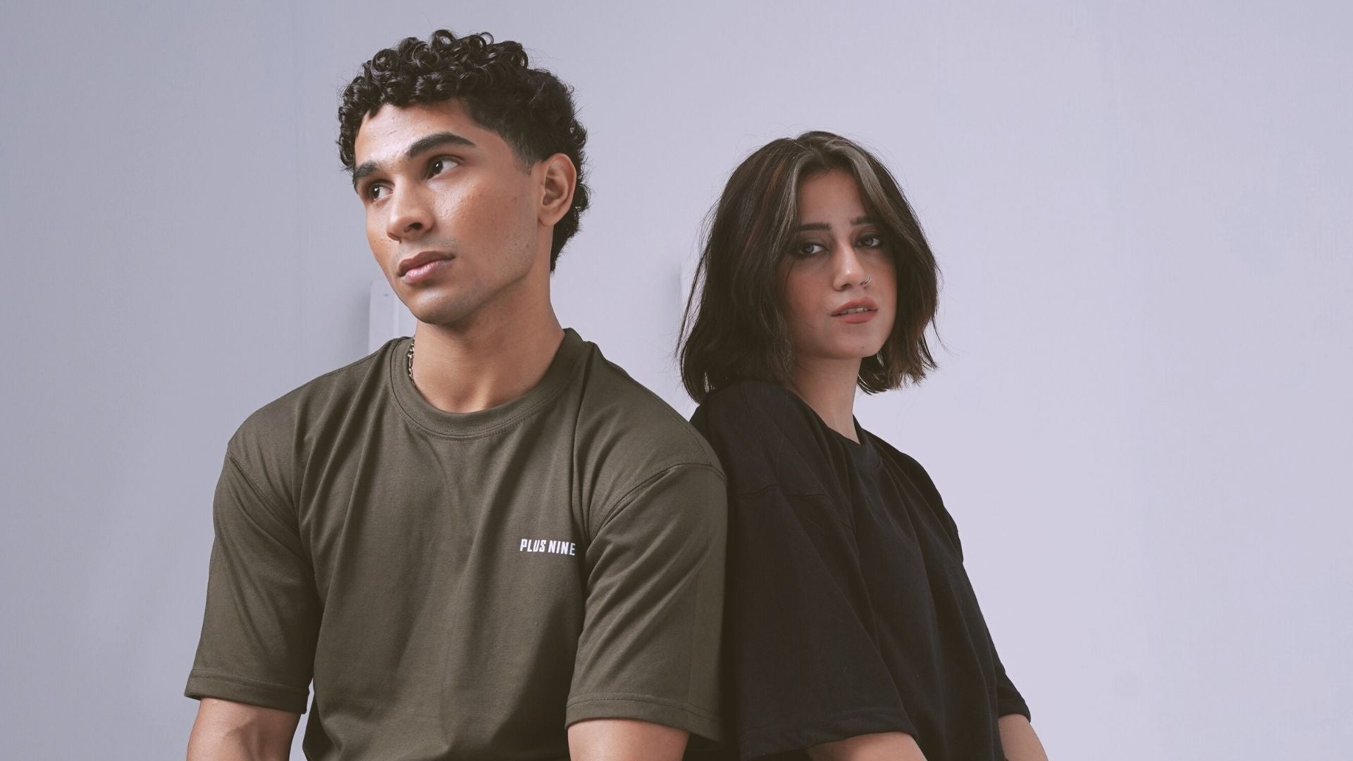 Two people standing side by side against a plain background wearing plus92 clothing Dropshirts