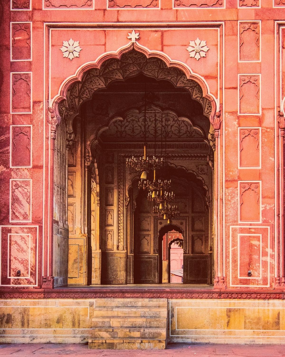 Ornate pink and gold archway with intricate designs and a chandelier inside.