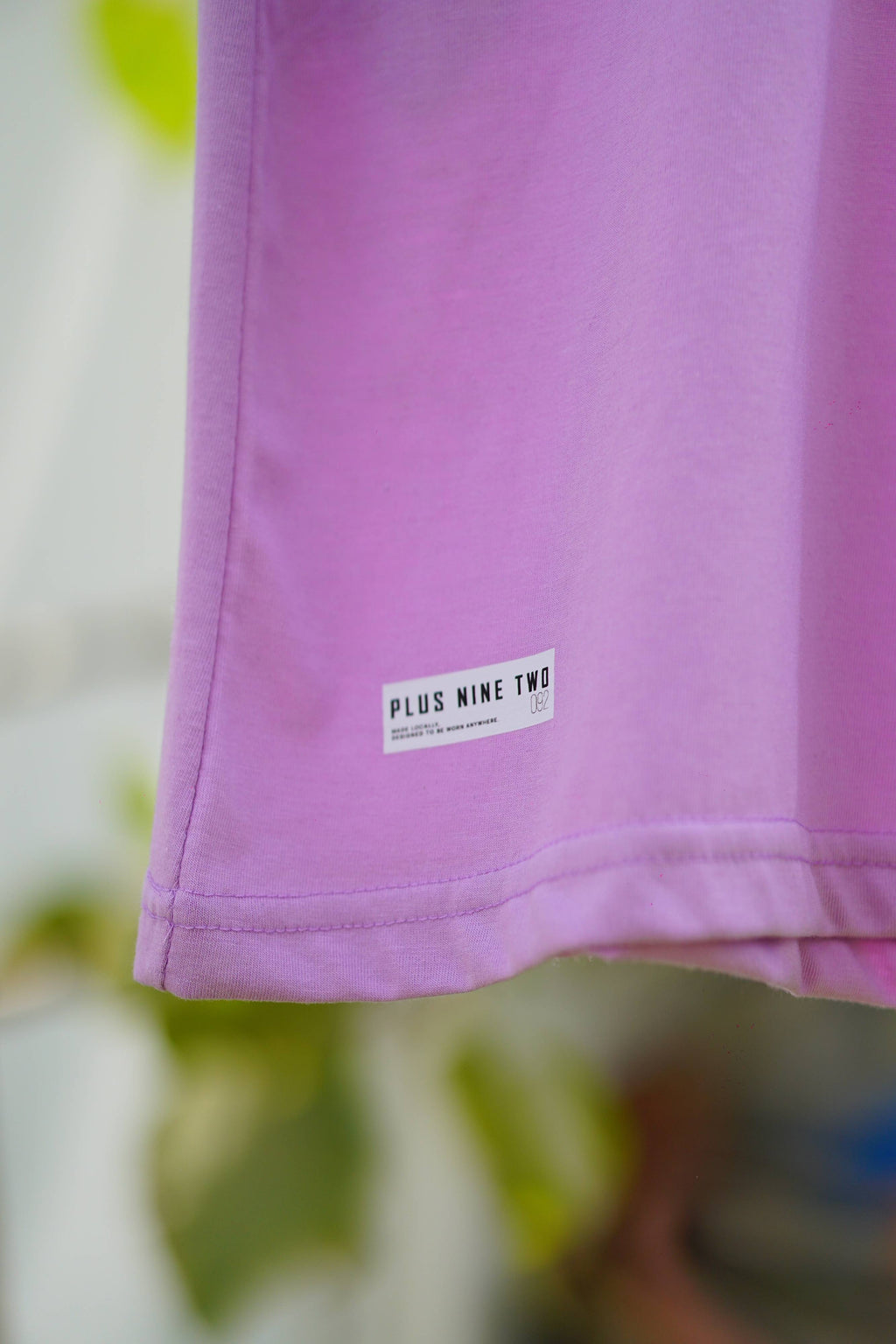 Close-up of the bottom hem on the Lahore Lilac Men's Essentials Drop Shirt, highlighting the white "PLUS NINE TWO" label.