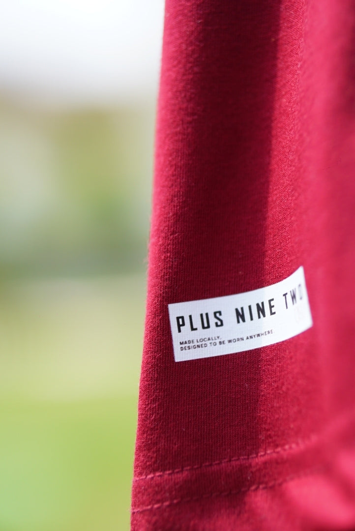 Close-up of the white label on the lower hem of the Ajrak Maroon Men's Essentials Drop Shirt.