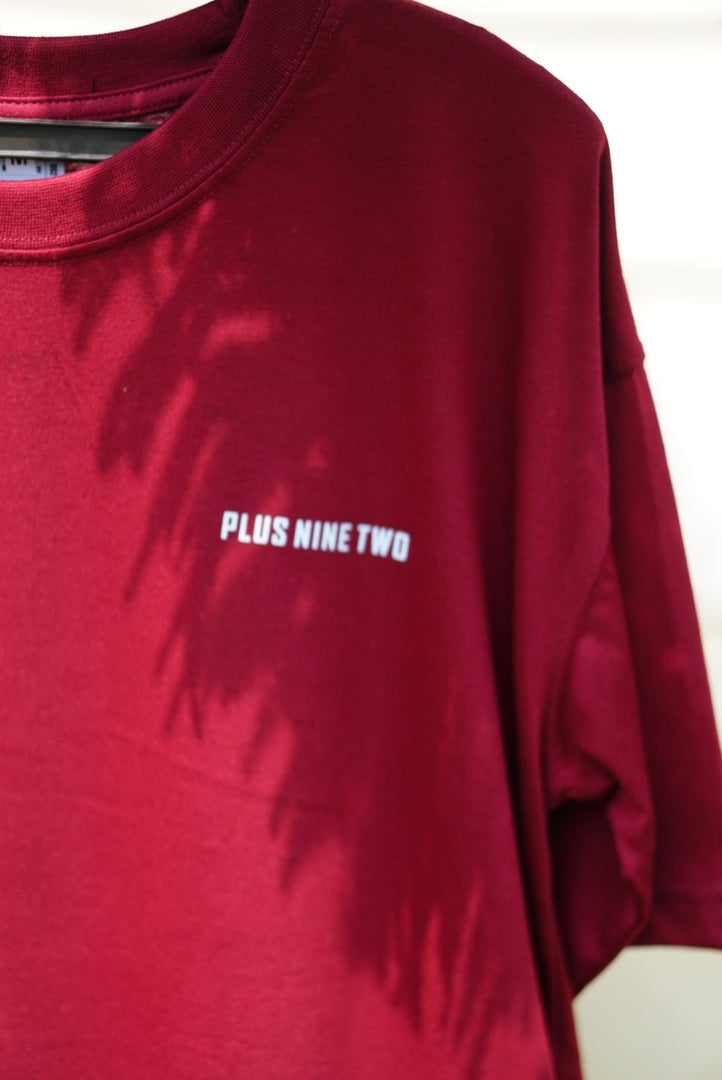 Detail shot of the chest logo on the Ajrak Maroon Men's Essentials Drop Shirt, featuring "PLUS NINE TWO" in white block letters.