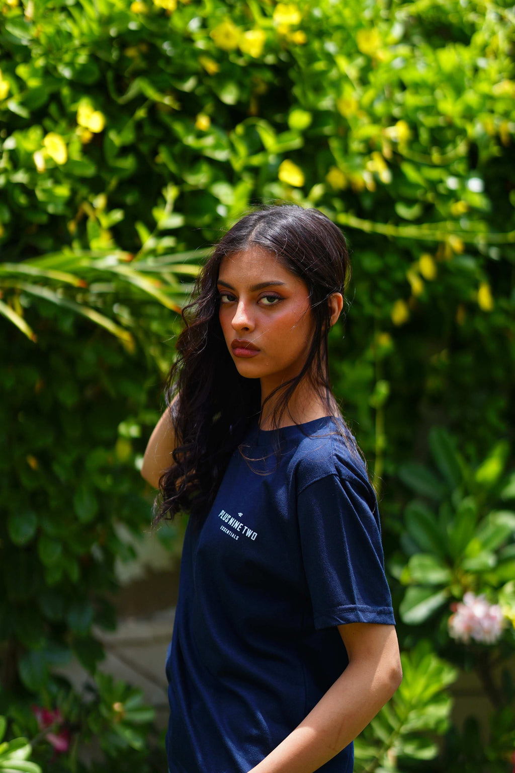 Girl wearing essentials indus navy blue blend t-shirt turned to show sleeve and looking towards the camera.