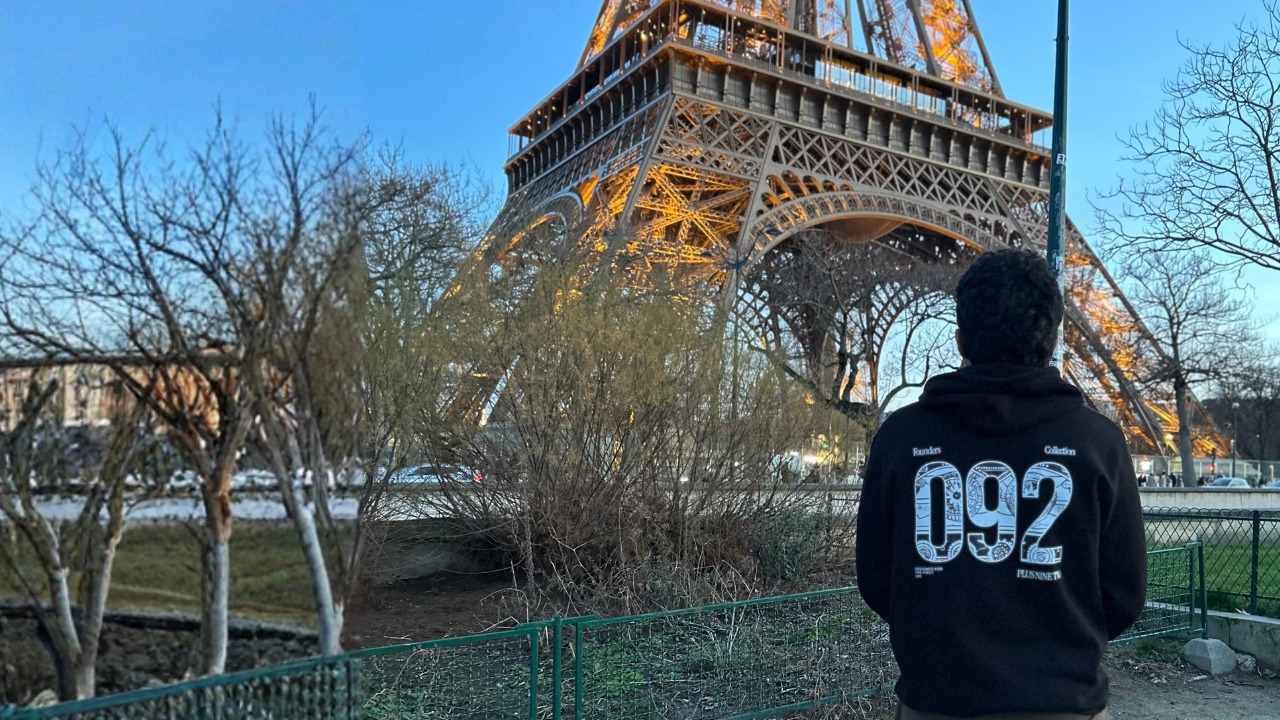 Person wearing a black hoodie with '092' on the back, standing in front of the Eiffel Tower.