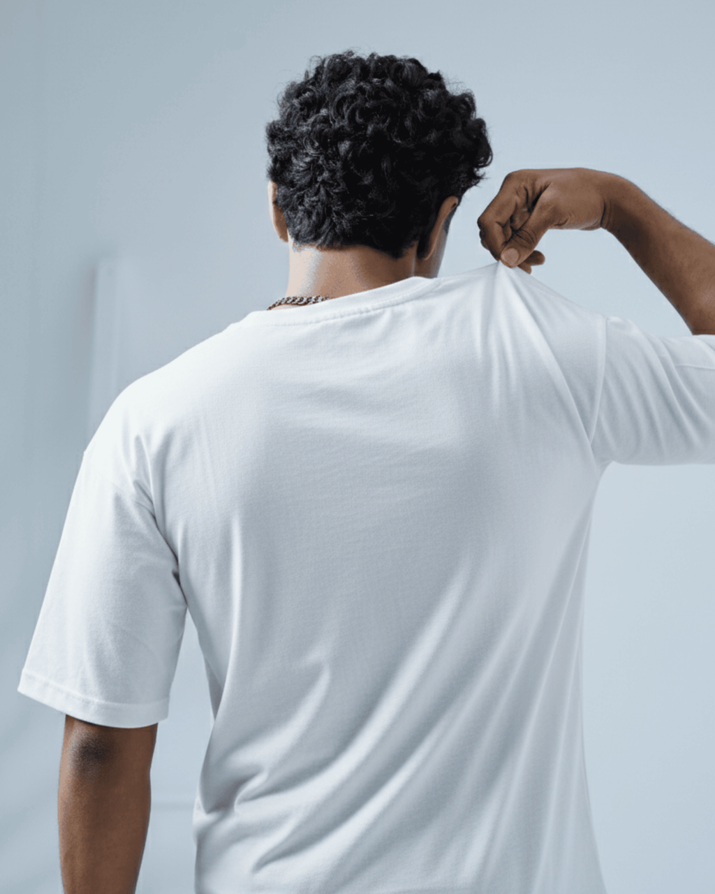Man wearing a white oversized t-shirt facing away from the camera against a light gray background