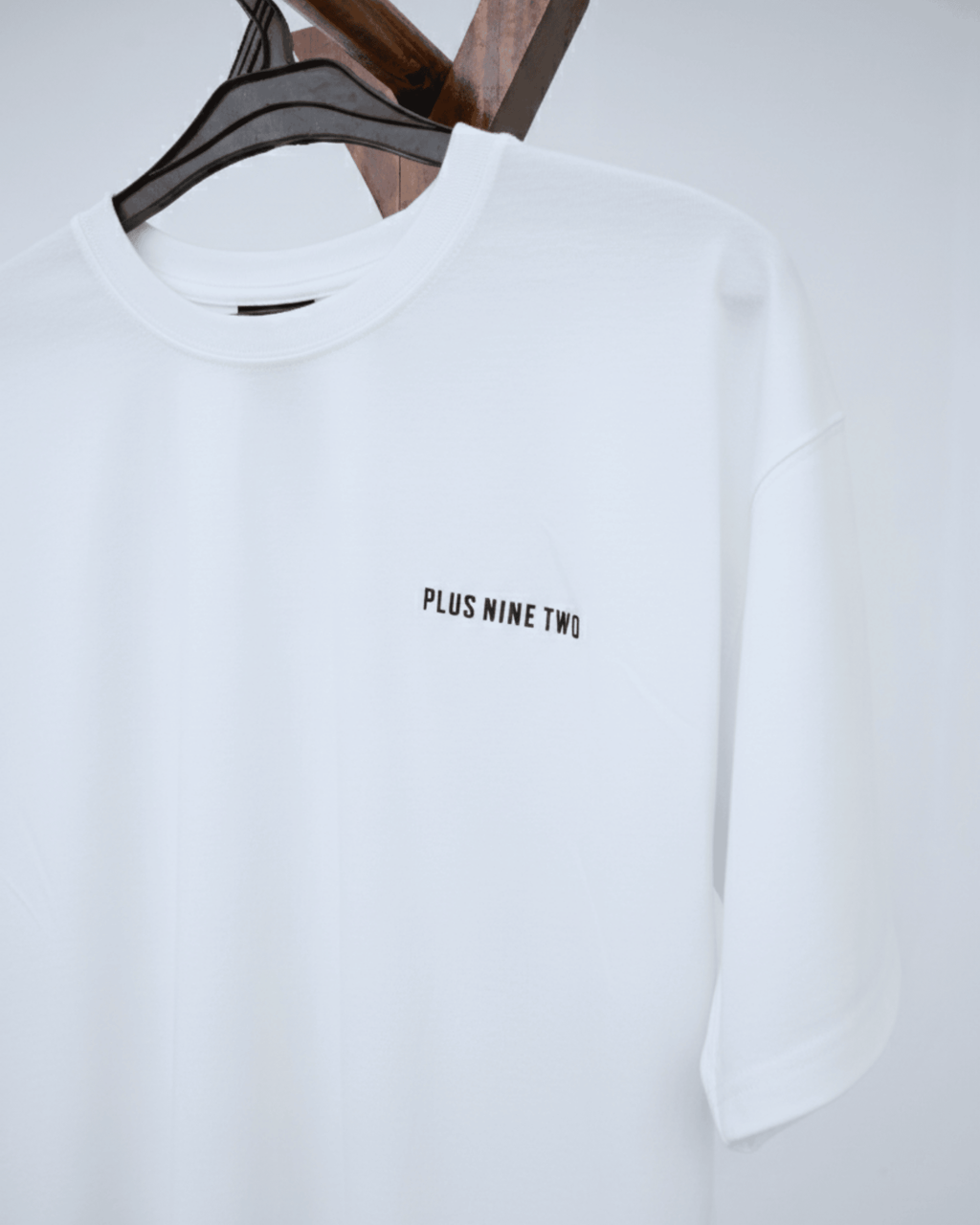 White oversized t-shirt with 'PLUS NINE TWO' text on a hanger against a white background