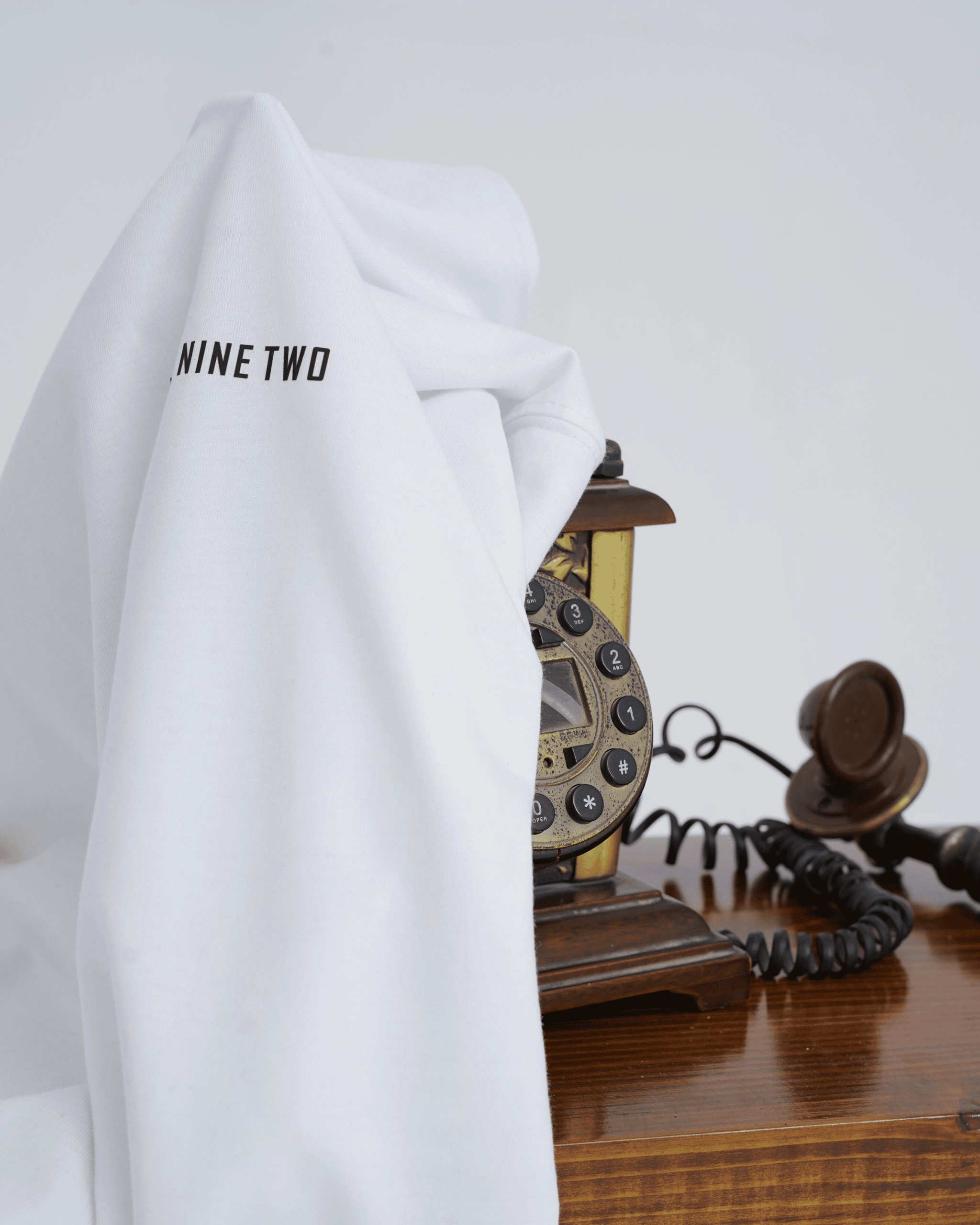 White oversized t-shirt with 'NINE TWO' showing from the logo draped over a vintage telephone on a wooden surface.