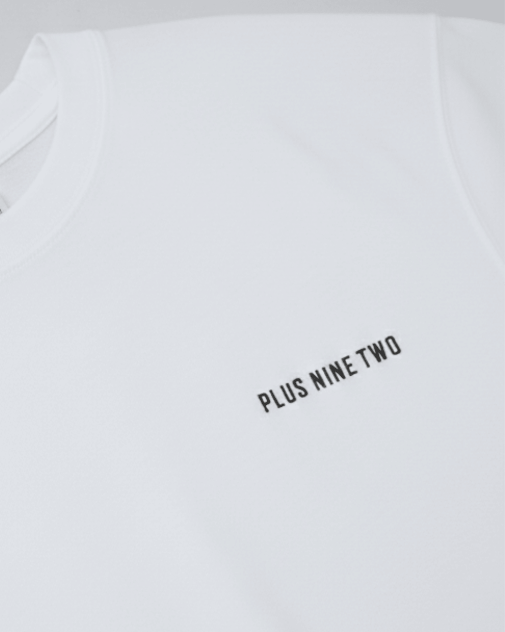 White oversized t-shirt with 'PLUS NINE TWO' text on a light gray background