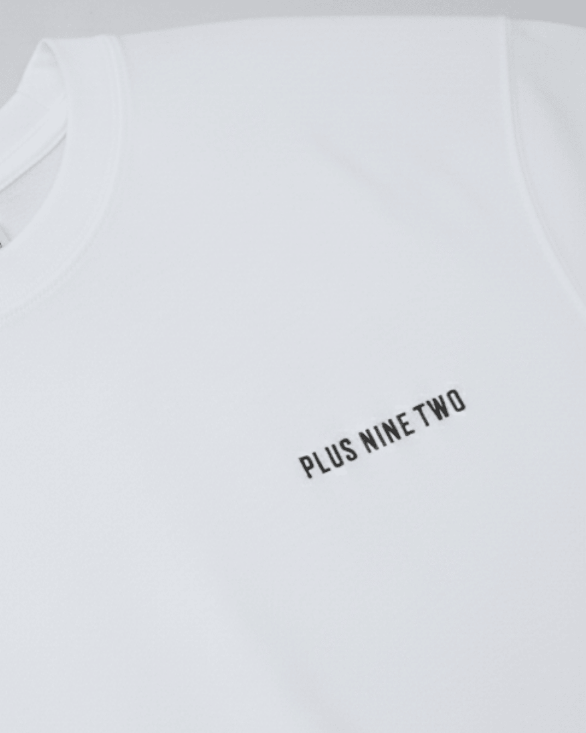 White oversized t-shirt with 'PLUS NINE TWO' text on a light gray background