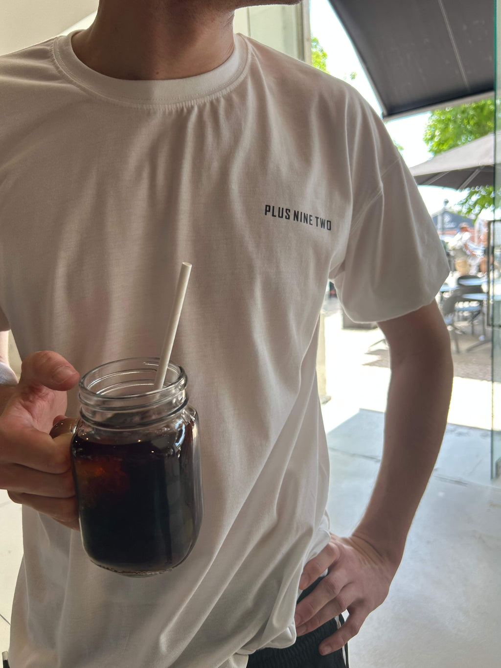 Man wearing plus92 clothing essentials white oversized t-shirt holding a cold brew.