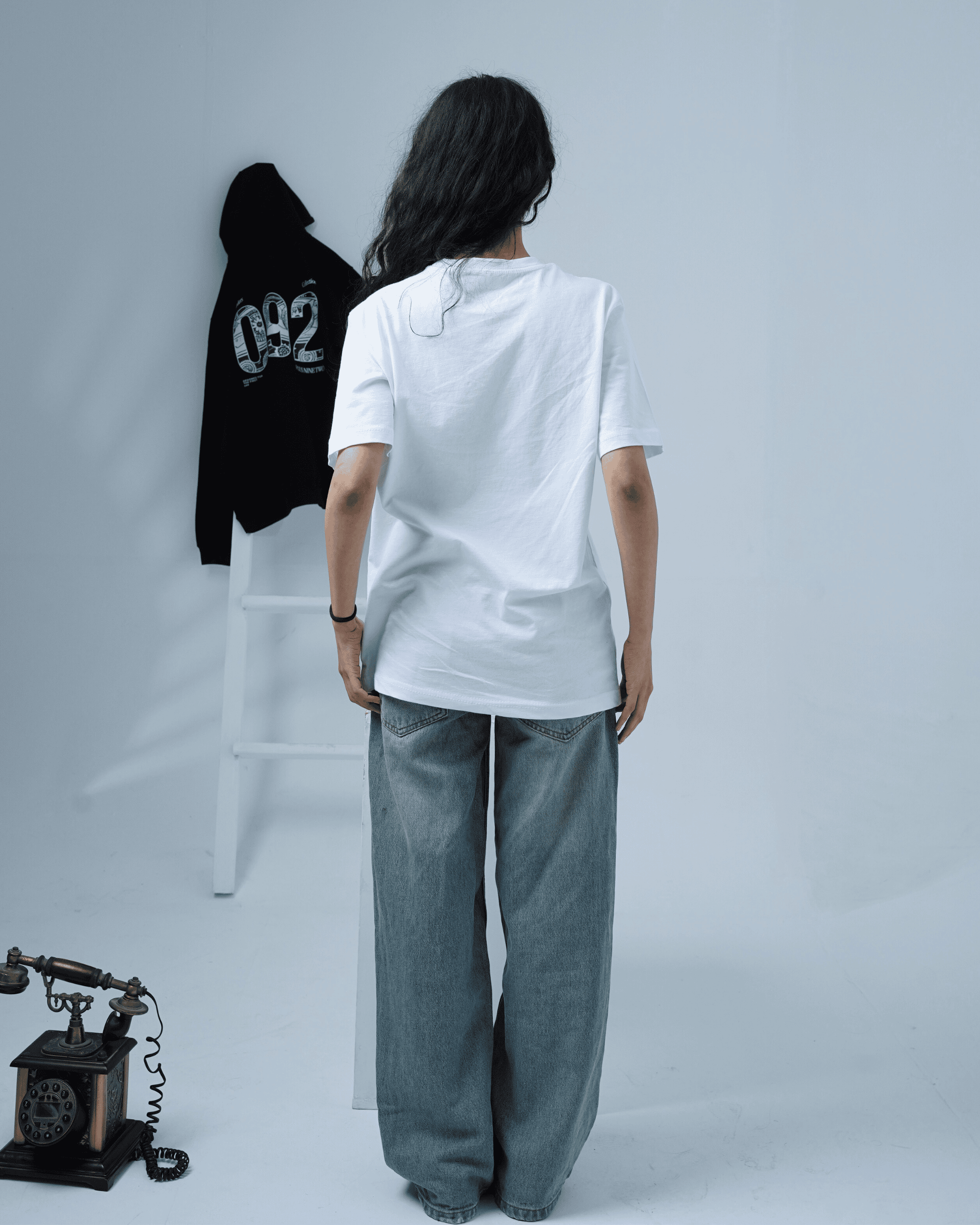 Girl standing with back facing the camera wearing a white t-shirt with founders edition hoodie in the background with '092' on a white background.