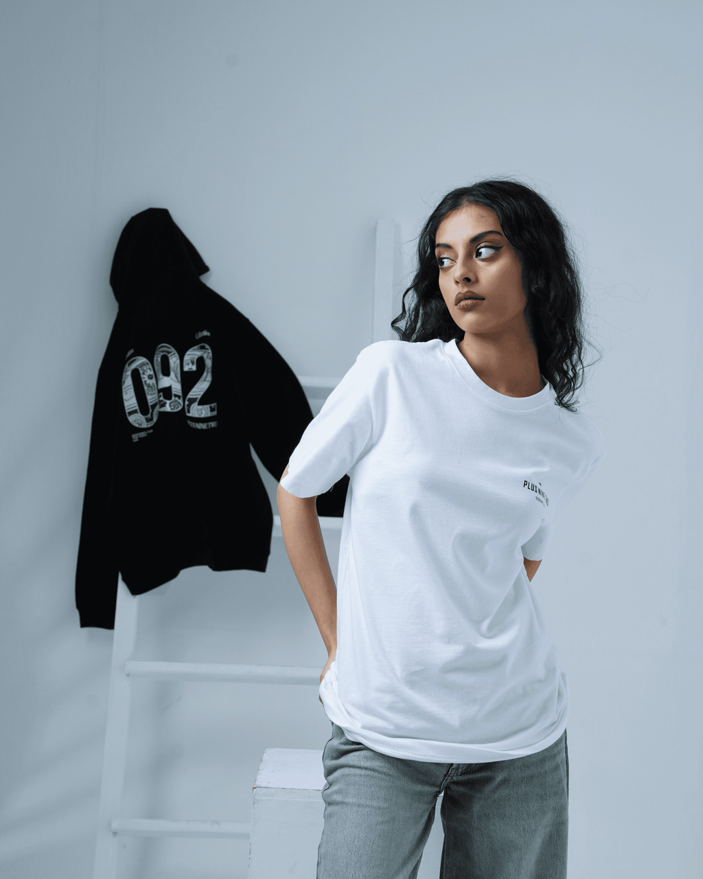 Woman wearing a white t-shirt with a black hoodie on a gray background