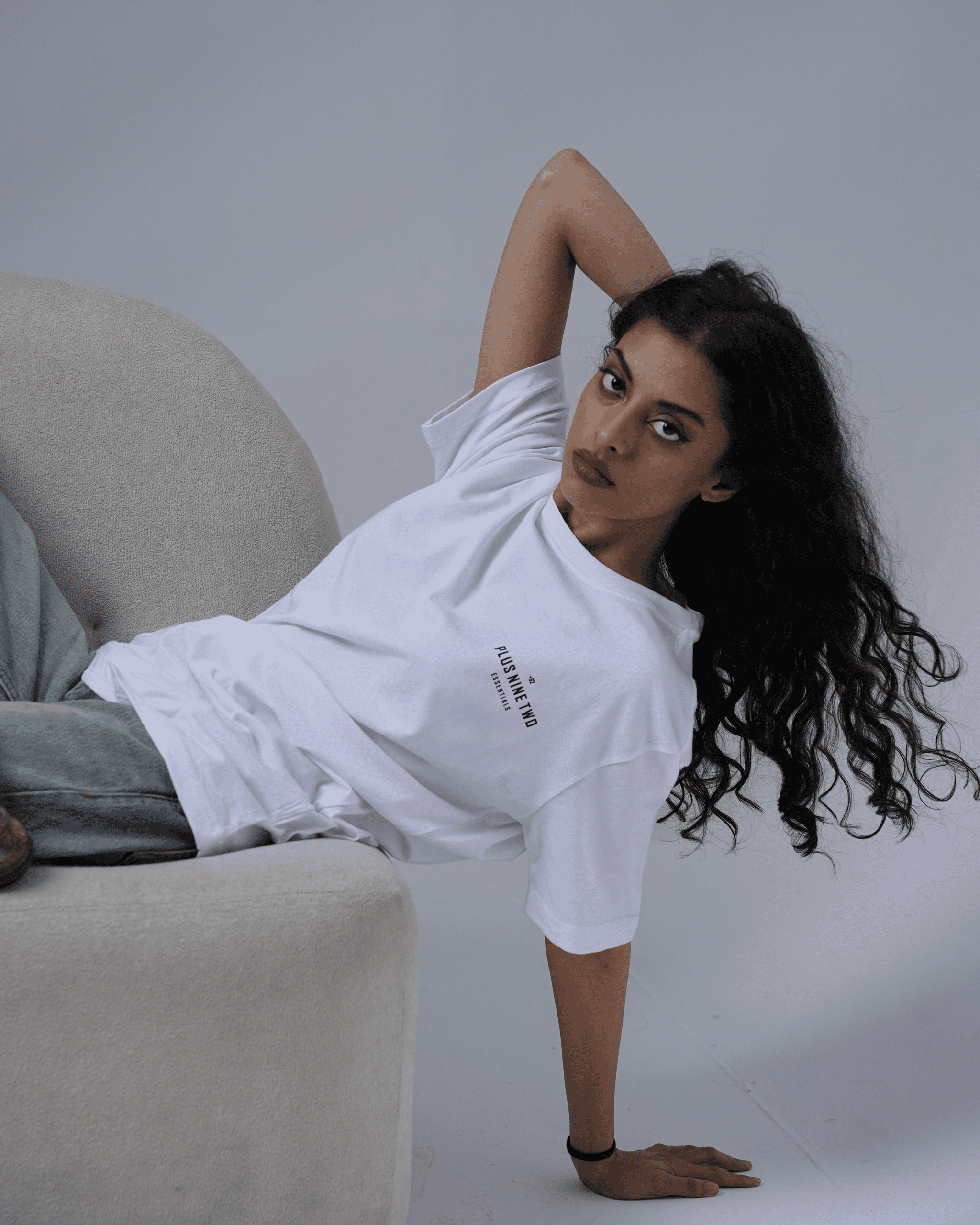 Woman in a white t-shirt sitting on a couch against a plain background