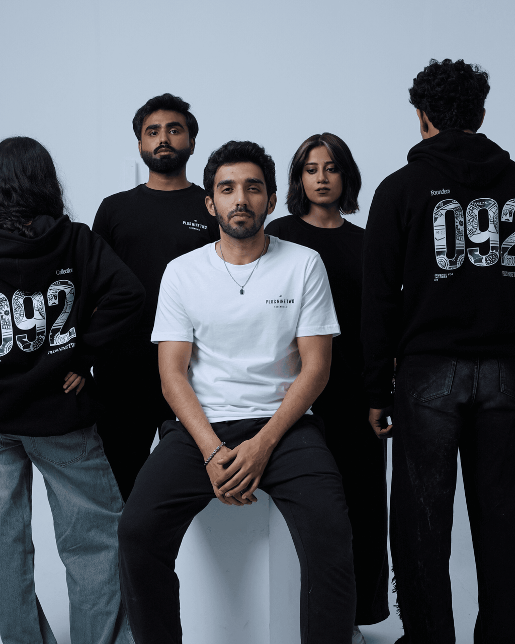 Group of people wearing different products of +92clothing standing around a person in a white shirt.