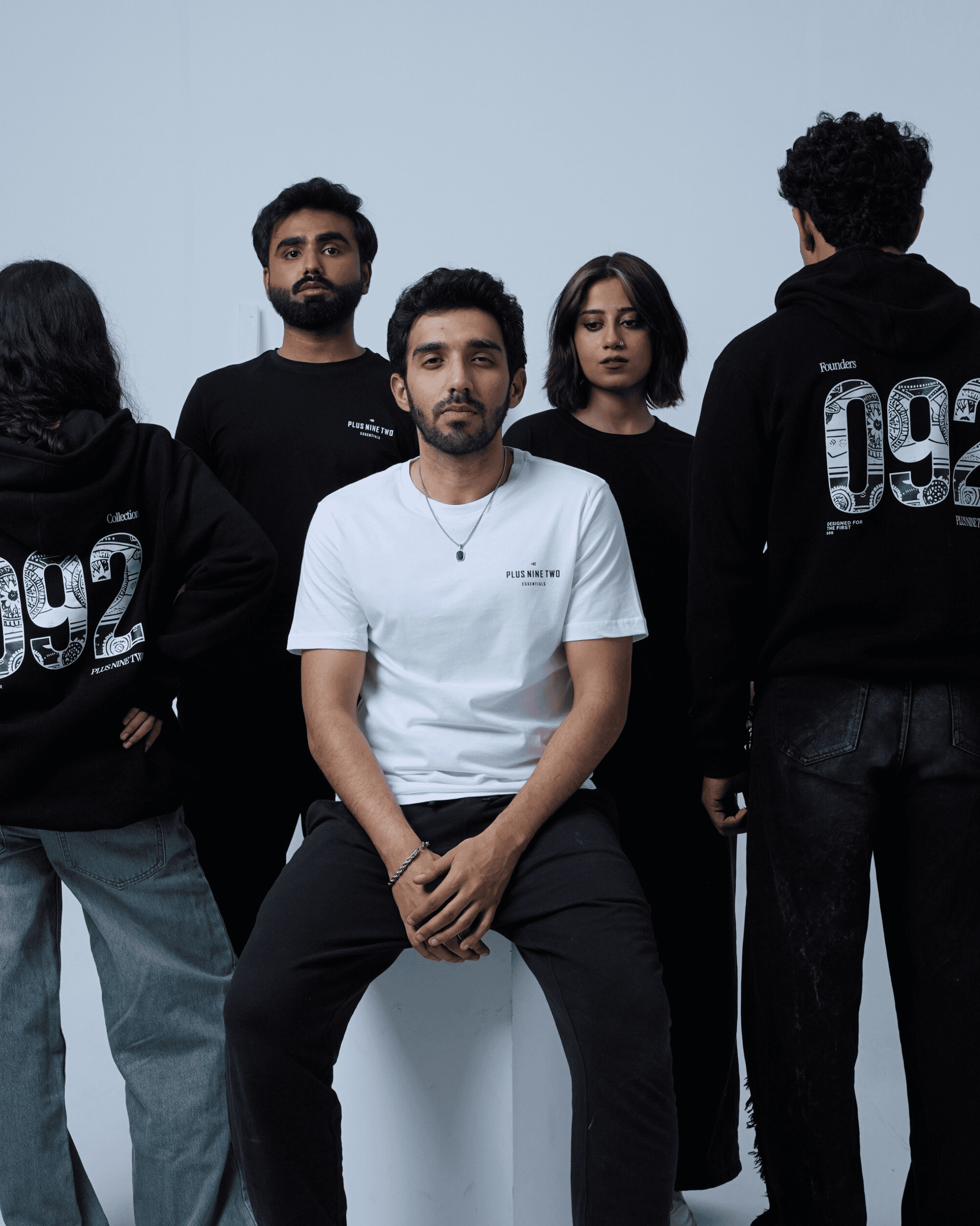 Group of people wearing different products of +92clothing standing around a person in a white shirt.
