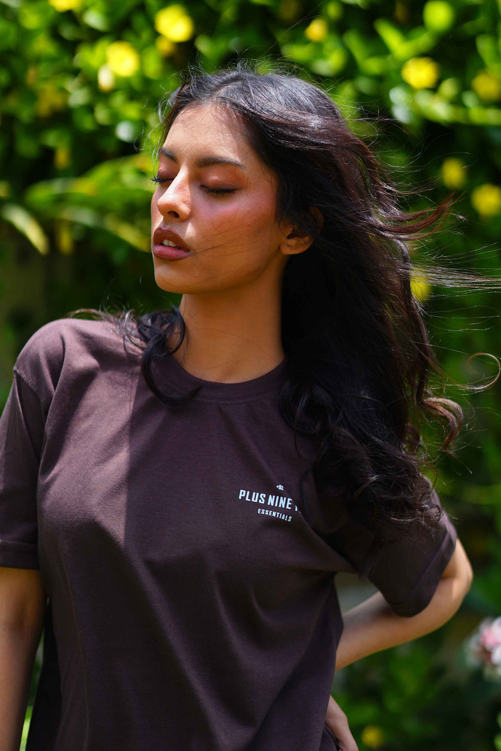 women standing in garden wearing essentials karak brown blend t-shirt with product focused on design on the pocket.