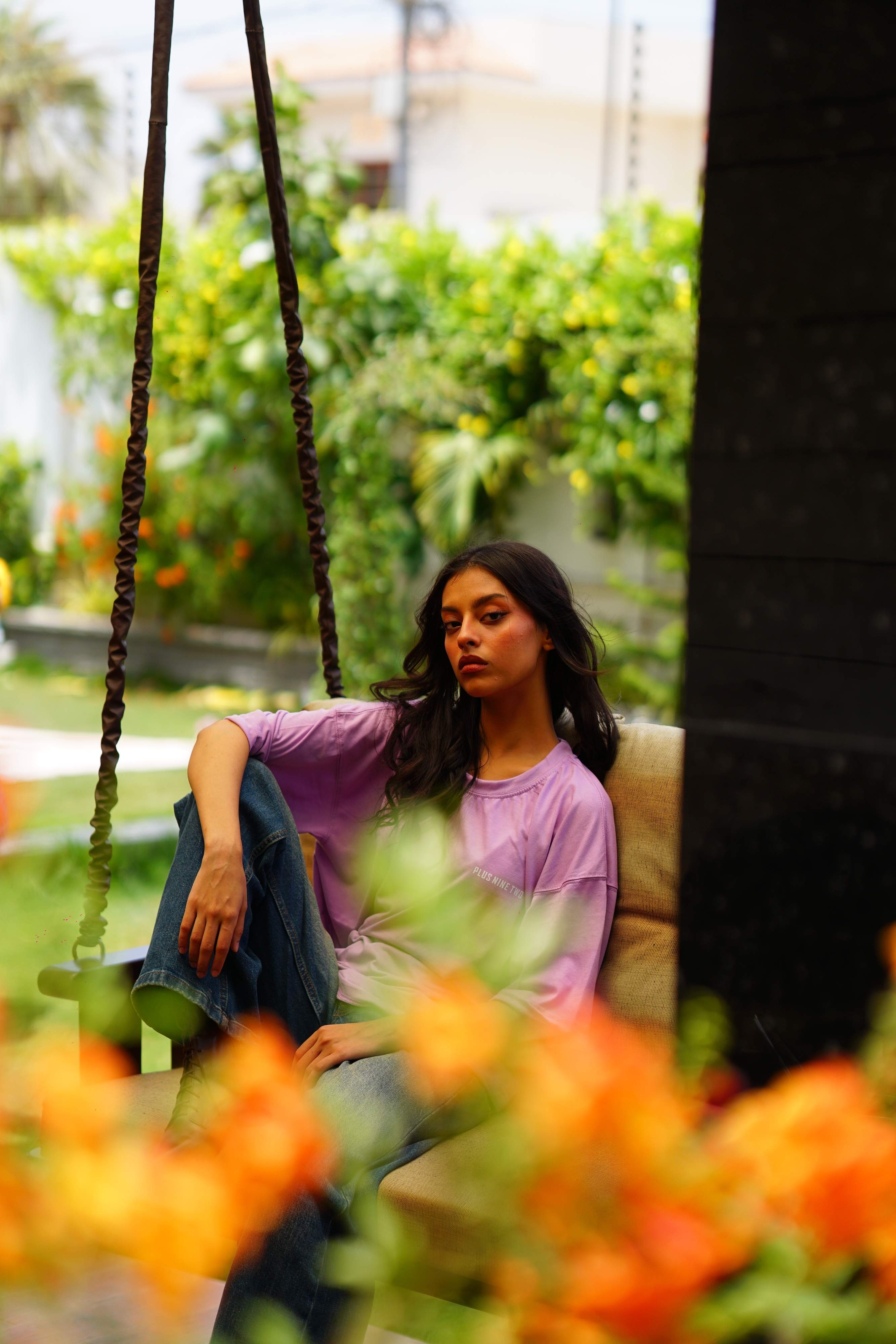 Female model wearing Lahore Lilac Plus Nine Two oversized t-shirt on garden swing